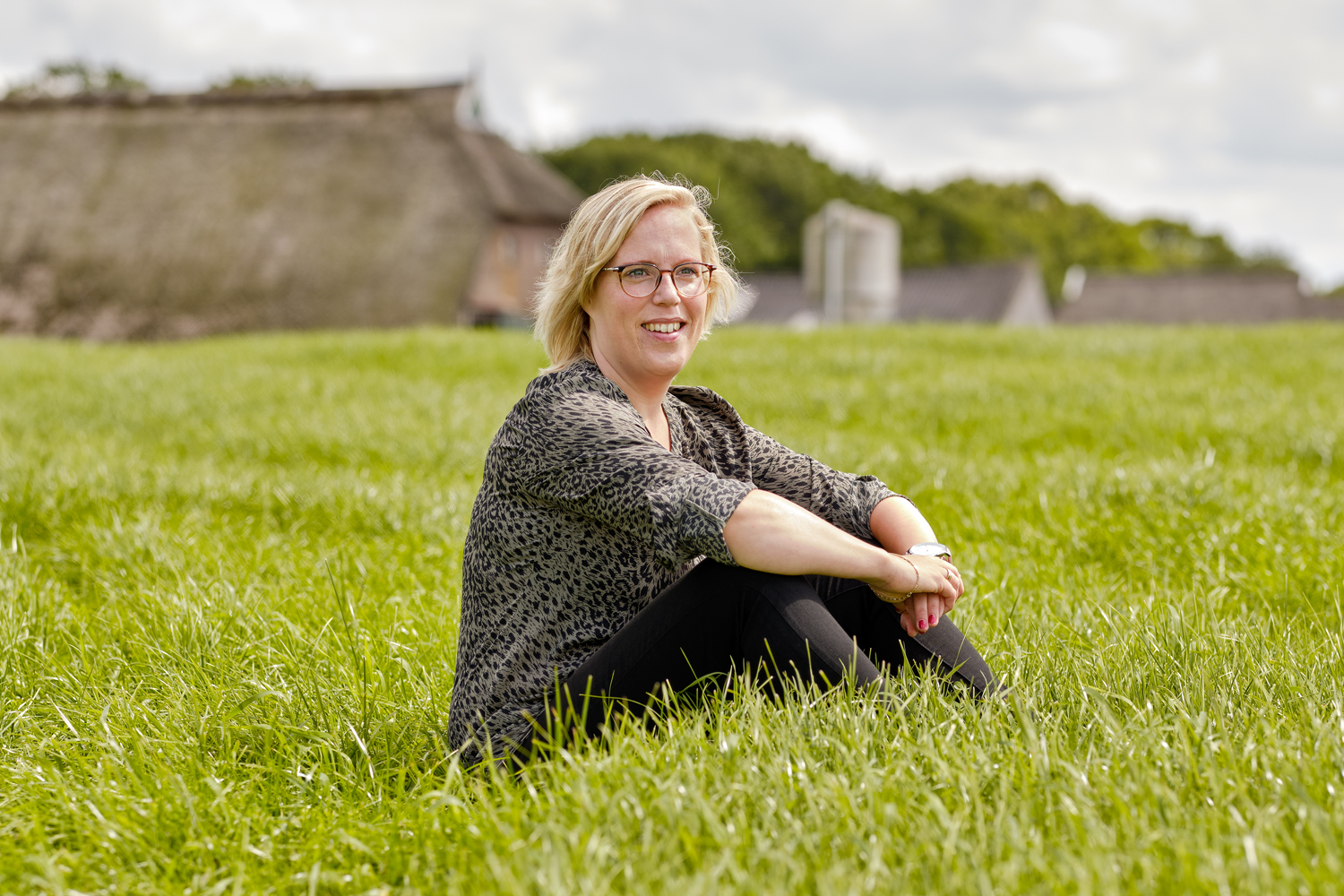 Blonde vrouw met bril zittend in gras